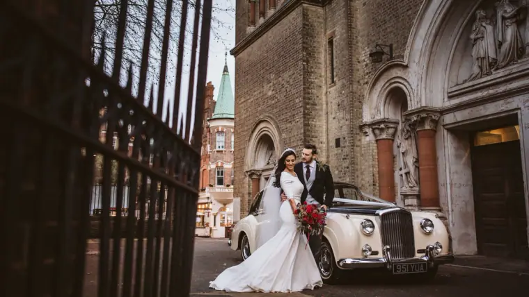 Bride and groom by a white vintage car outside a Gothic stone church