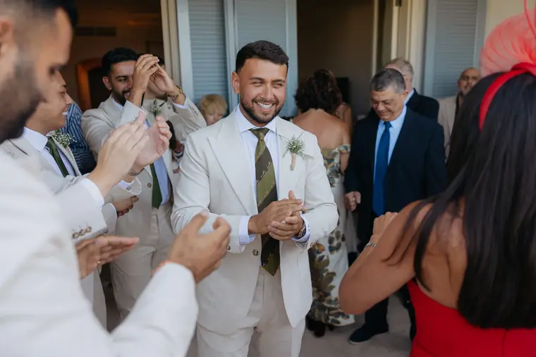 Andrew in a cream suit surrounded by applauding family and groomsmen