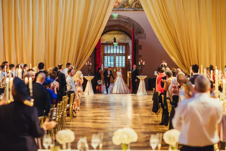 Bride and groom entering the reception between golden drapes as guests applaud