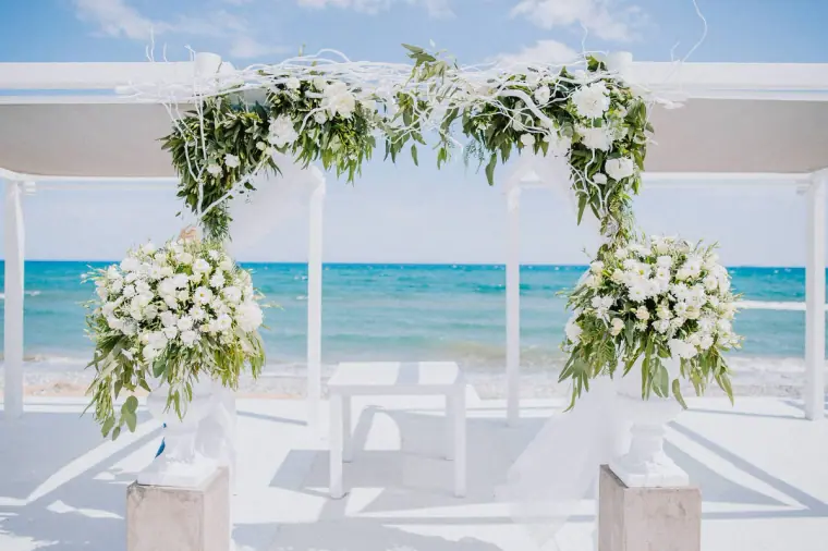 White floral ceremony arch on a terrace overlooking a turquoise sea at Galu Seaside, Larnaca