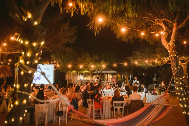 Outdoor reception tables beneath pine trees strung with festoon lights, Thalassines Beach Villas
