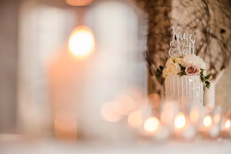 Wedding cake with a "Kaye & Matt" topper behind glowing candles, softly blurred