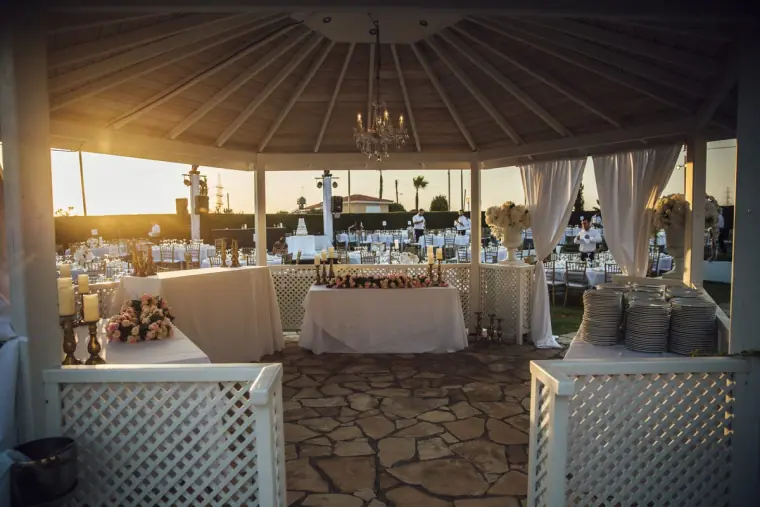 Gazebo with white drapes and lattice framing the reception tables at sunset