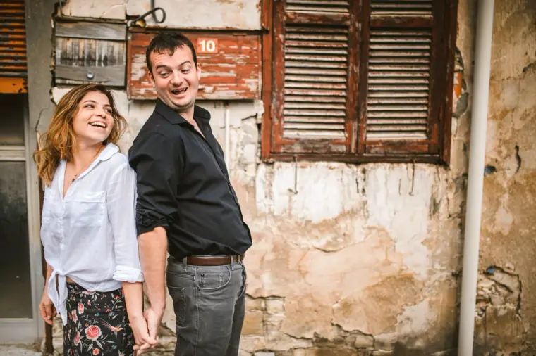 Couple laughing beneath old wooden shutters on a crumbling wall in Lefkara