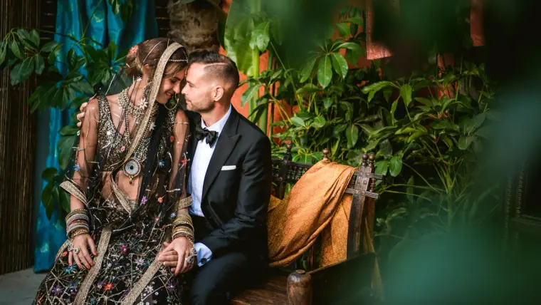 Bride in embroidered bridal wear and groom in a tuxedo among plants
