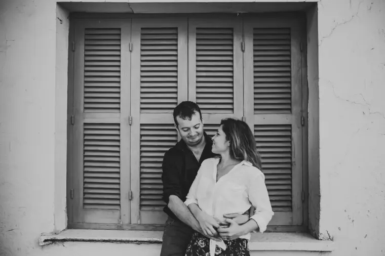 Black-and-white photo of the couple embracing in front of closed shutters