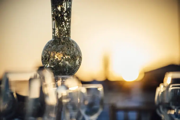 Sun setting behind glassware and a mirrored centrepiece on a reception table