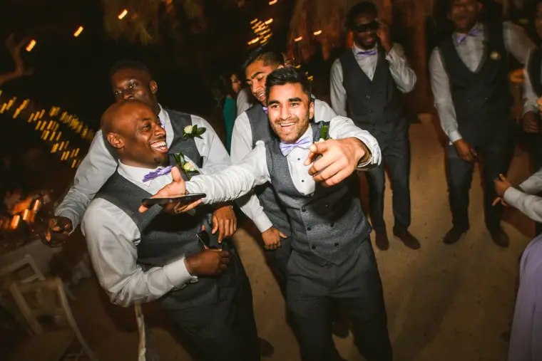 Groomsmen dancing energetically on the sandy dance floor at night