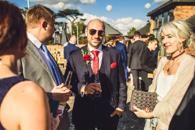 Groomsman in sunglasses with a red tie chatting with guests in the sun