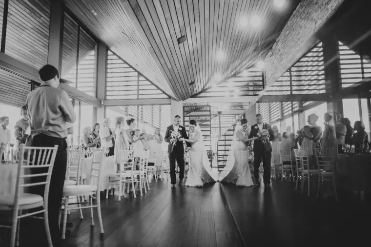 Black-and-white photo of guests standing as the newlyweds enter the dining room