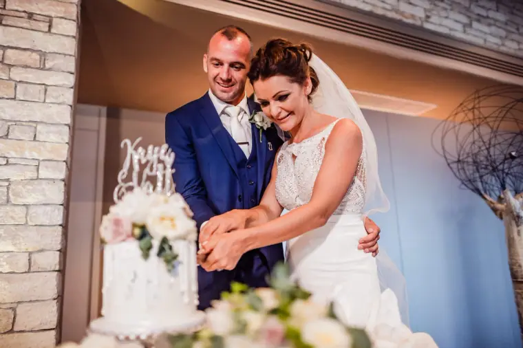 Couple cutting the white wedding cake together, laughing
