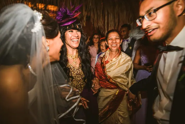 Bride laughing with guests, including a woman in a purple fascinator, during the party