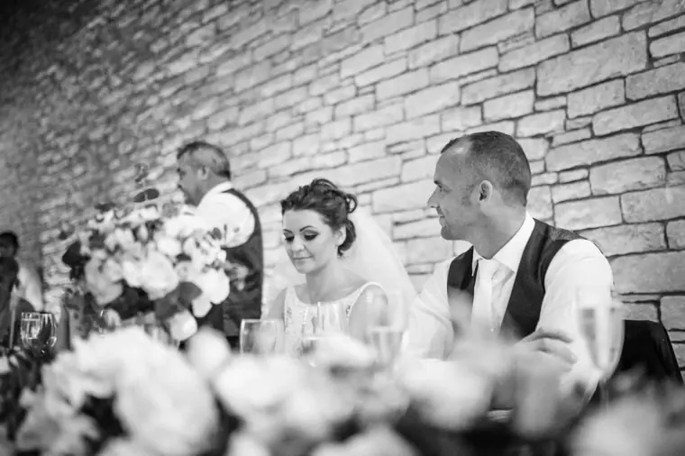 Black-and-white photo of the couple listening to speeches at the top table