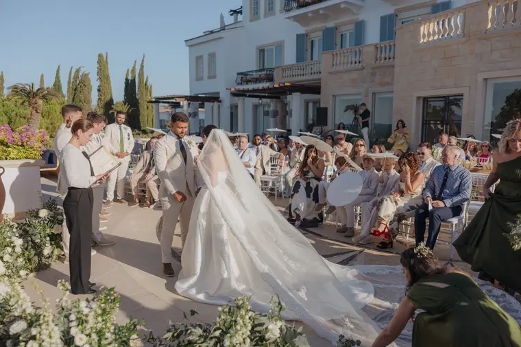 Poppy walking up the aisle with her long veil trailing as guests watch