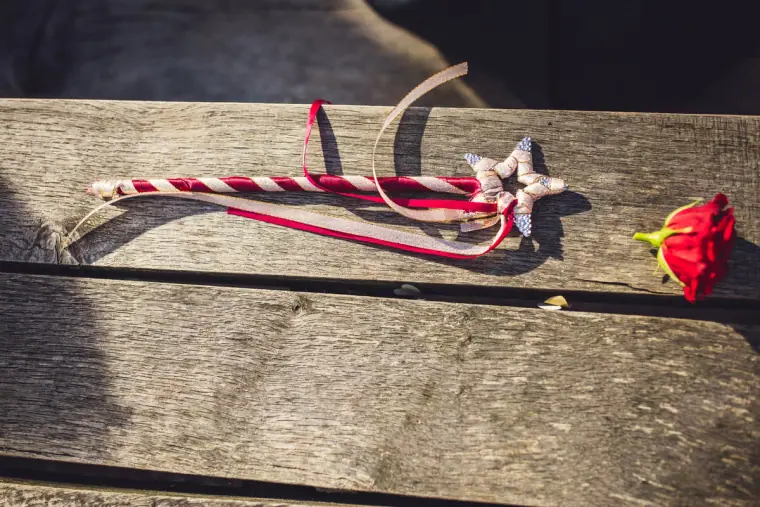 Candy-striped star wand with ribbons and a red rose on a wooden bench