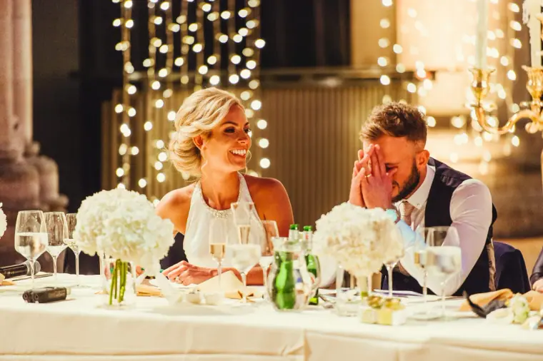Groom covering his face in laughter beside the bride at the top table