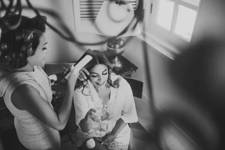 Black-and-white photo of a bride laughing as her hair is styled, Anassa