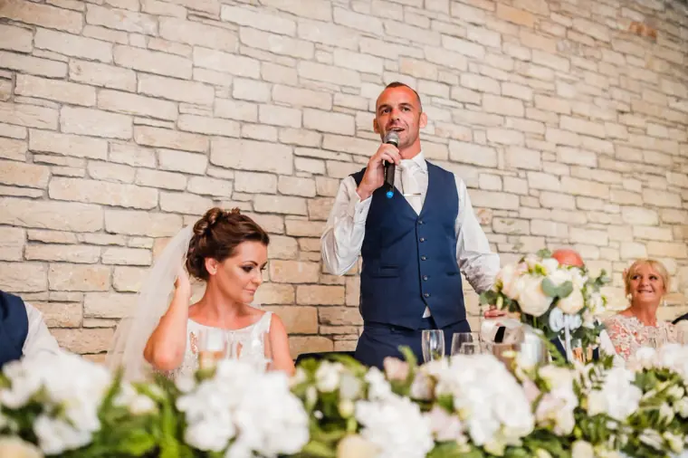 Groom giving his speech into a microphone beside the bride at the top table