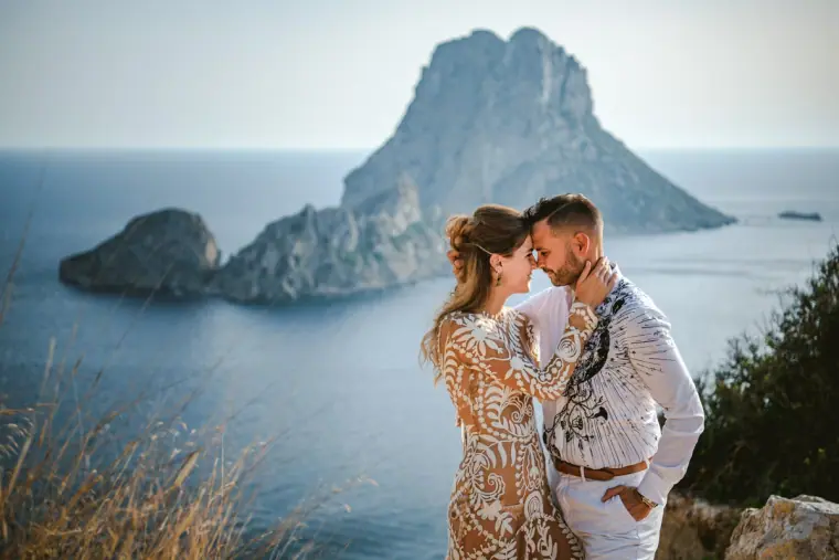 Couple touching foreheads on a clifftop facing a towering rocky islet