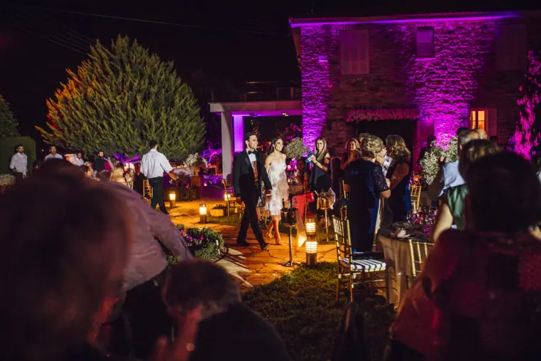 Newlyweds arriving among guests under purple-lit stone walls at night