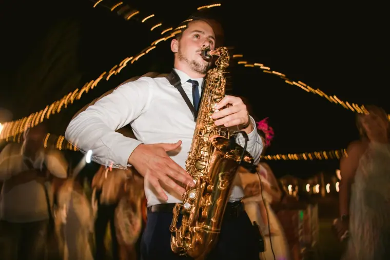 Saxophonist in a white shirt performing under string lights at night