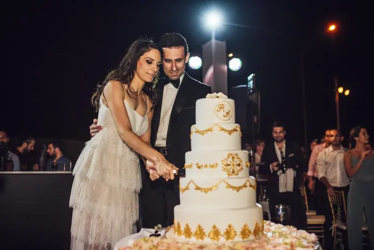 Ruby and Angelos cutting their gold-detailed wedding cake at night