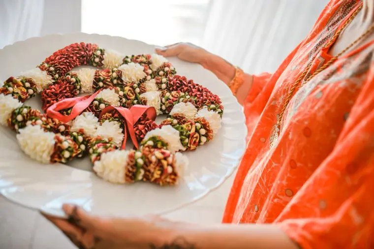 Woman in an orange sari holding a plate of red and white flower garlands