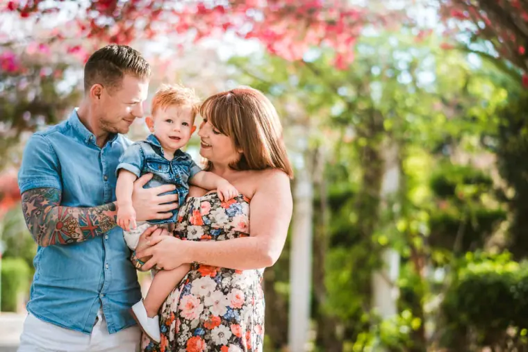 Couple holding their toddler beneath pink flowering trees