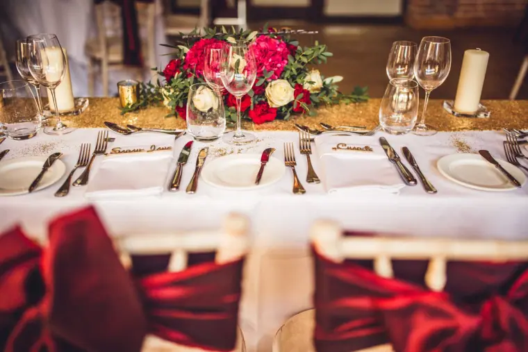 Reception table set with red roses, glassware and burgundy chair sashes