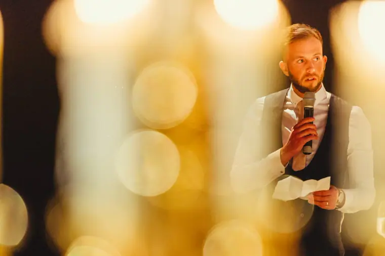 Best man giving his speech with a microphone, framed by blurred candlelight
