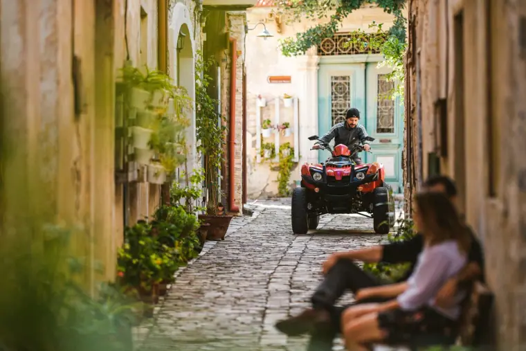 Couple sitting on a bench in a cobbled lane as a quad bike approaches