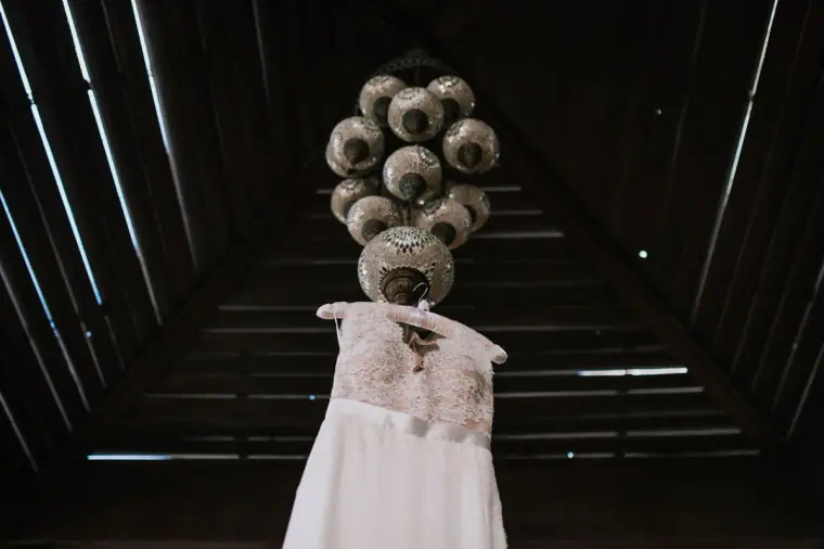 Wedding dress hanging beneath an ornate silver lamp in a dark timber-roofed room, Hadjiantonas Winery