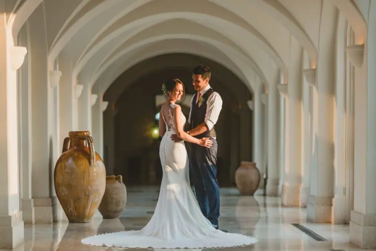 Kat and George embracing in a white arched colonnade with terracotta urns at Anassa