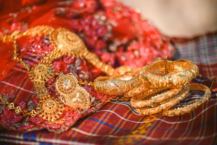 Gold bangles and necklace resting on folds of a red embroidered sari