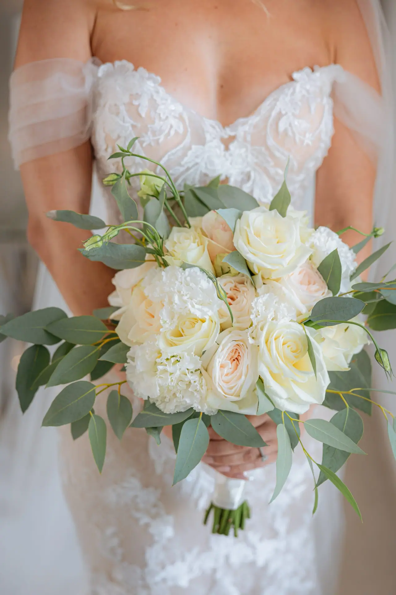 Close-up of an off-the-shoulder lace gown and white rose bouquet
