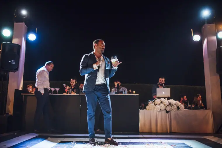 Guest in a blue suit giving a speech on the lit dance floor at night
