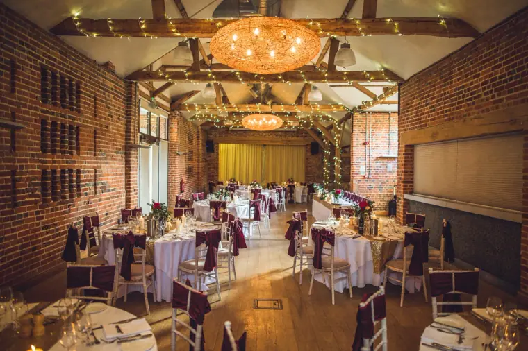 Barn reception room with chandeliers and exposed beams set for dinner at Wasing Park