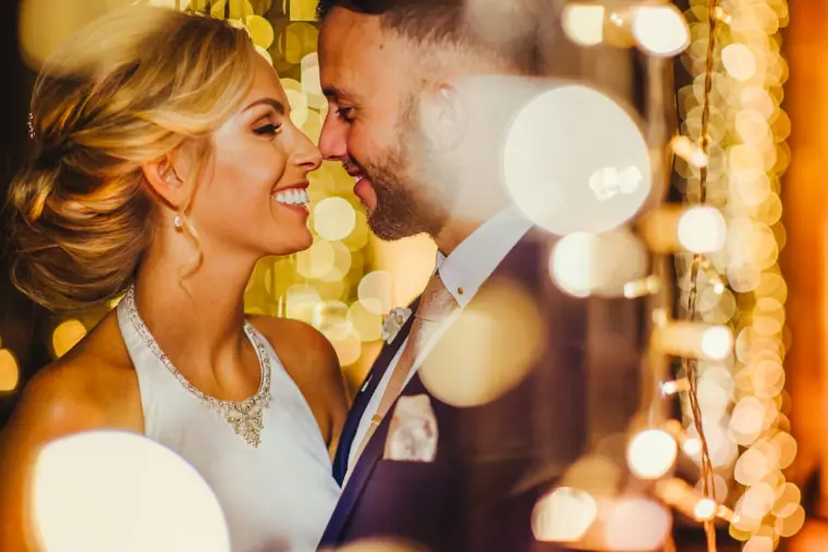 Bride and groom nose to nose, smiling among sparkling lights