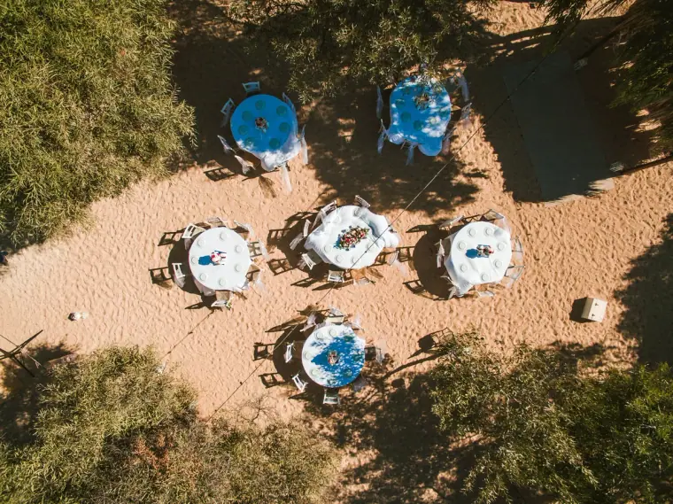 Aerial view of round dining tables laid on the sand between pine trees