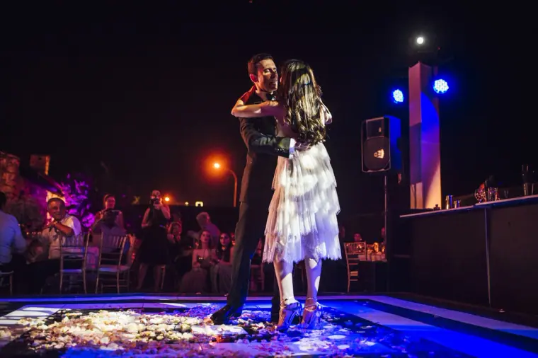 Bride and groom in a close embrace on the lit dance floor among guests