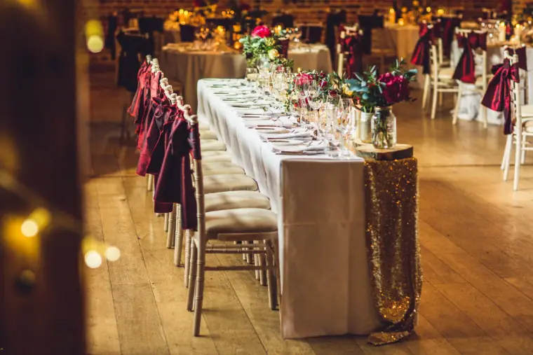 Long reception table with gold sequin runner and burgundy chair bows