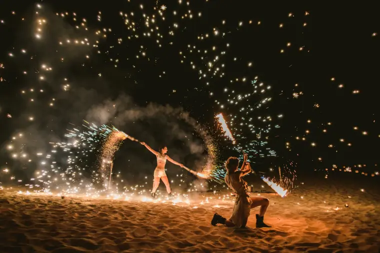Fire dancers spinning sparks on a beach at night