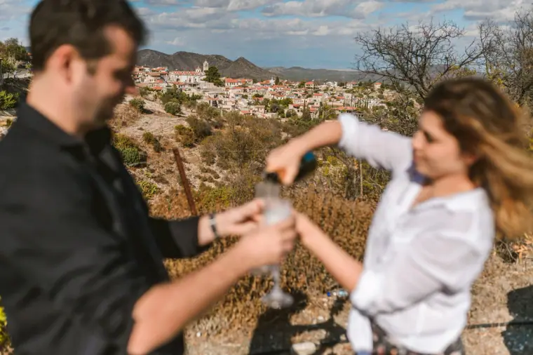 Couple popping a bottle of fizz on a hillside above the village
