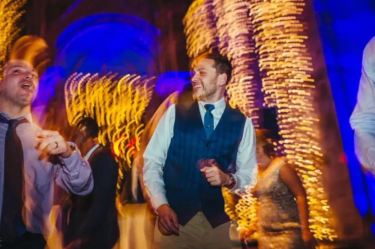 Guests in waistcoats dancing beneath blurred golden lights