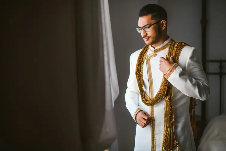 Adhib in his cream and gold sherwani standing in soft window light