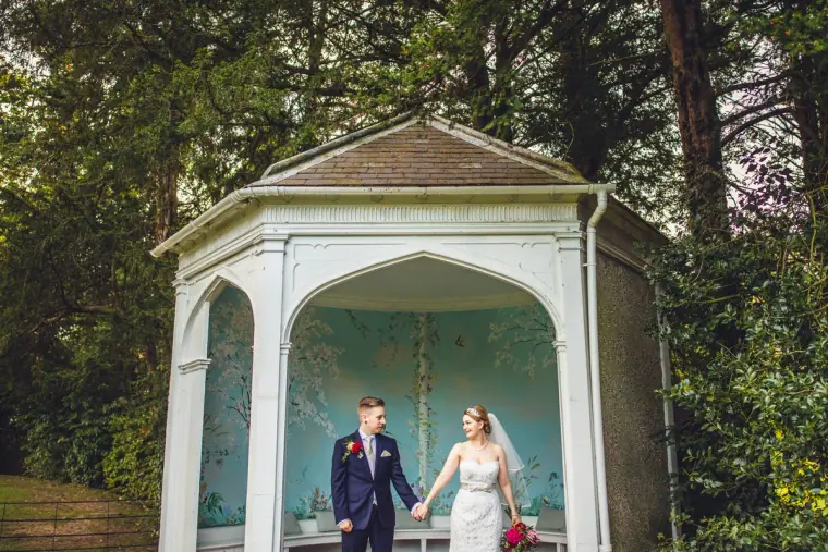 Sarah and Charlie holding hands in the white gazebo among the trees