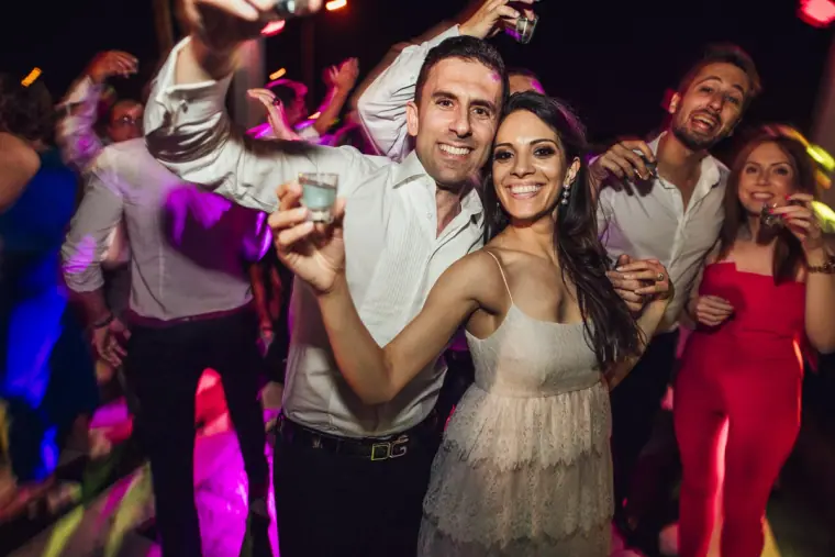 Groom and bride celebrating with shot glasses among friends at night