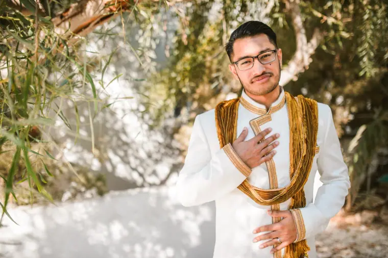 Groom in his sherwani with his hand on his heart, smiling among olive branches