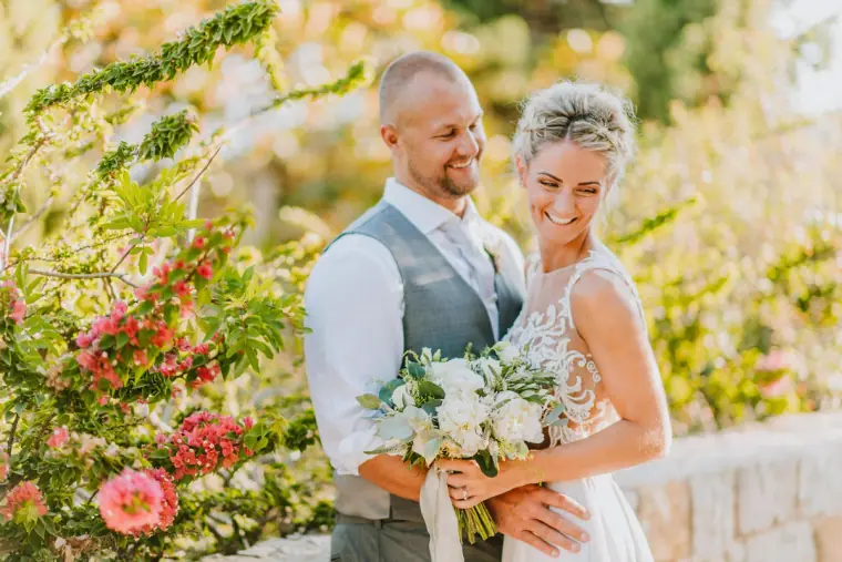 Kirsten and Samuel smiling cheek to cheek among flowering shrubs at Aphrodite Hills