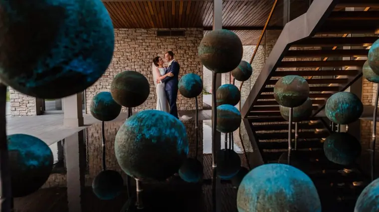 Bride and groom framed by teal sphere sculptures and a stone staircase in the Minthis Hills lobby, Tsada